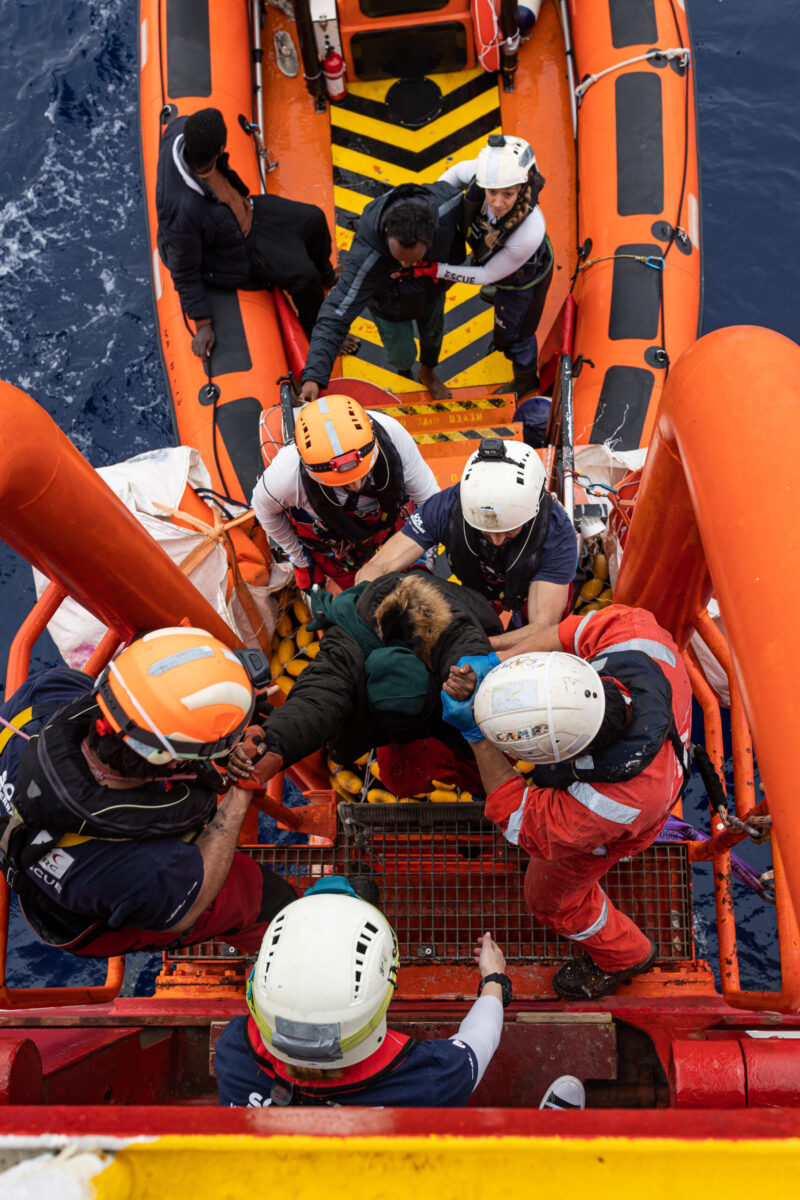 rescue workers helping a migrant into a rescue boat
